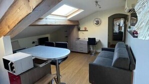 En kompakt opholdsstue med tekøkken, spiseplads og sofa.