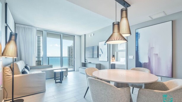 A modern living room with a round dining table, grey upholstered chairs, and pendant lighting.