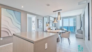 A modern kitchen with a central island, dining area with a round table, and a balcony with a view of the ocean.