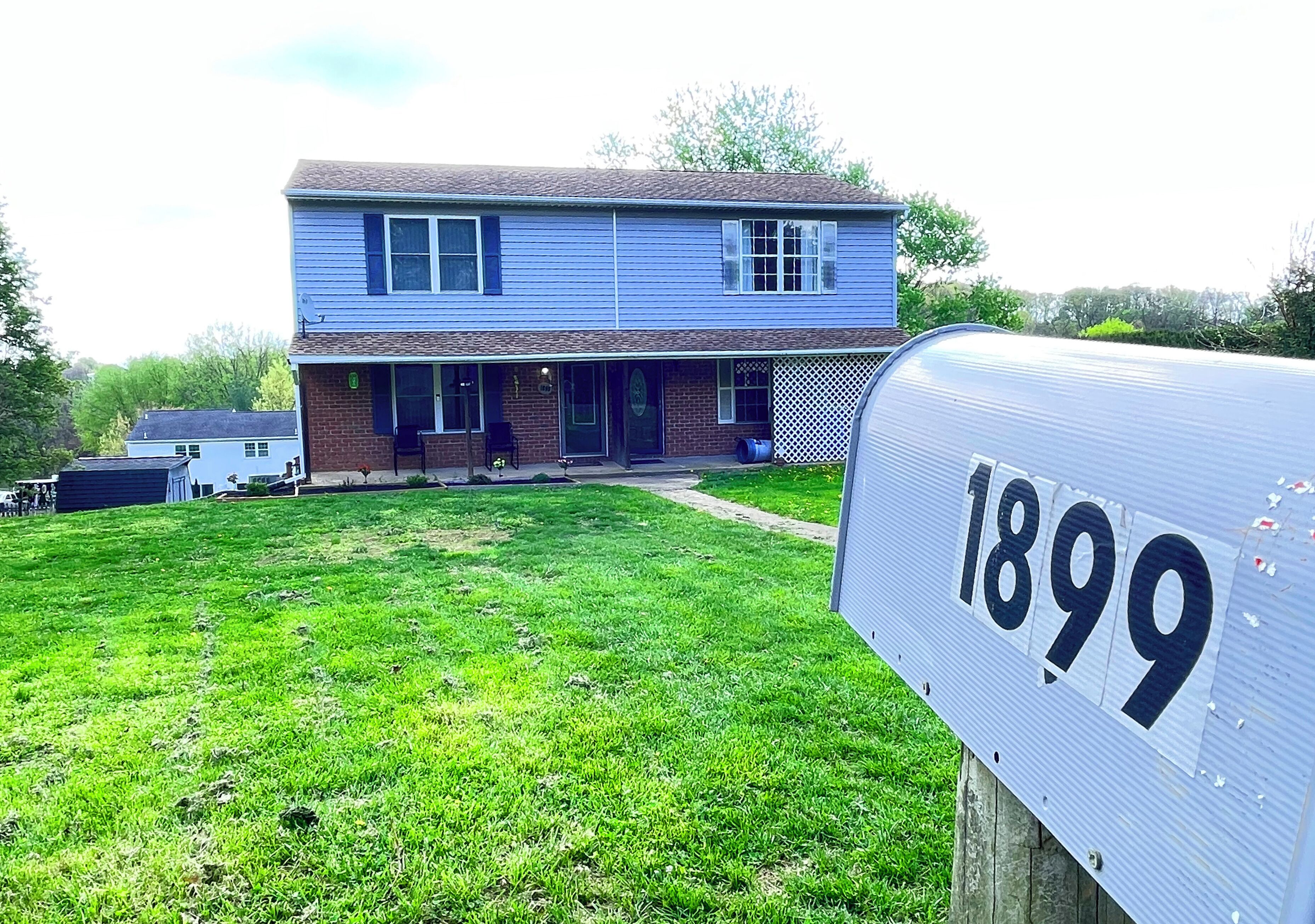 A two-story house with a front porch, a mailbox with the number 1899, and a grassy yard.
