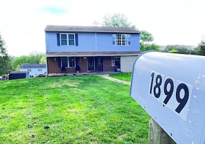 A two-story house with a front porch, a mailbox with the number 1899, and a grassy yard.
