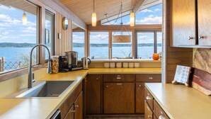 A modern kitchen with wooden cabinets, a stainless steel sink, and a view of a lake. - Beachfront I Tiki lounge | Pool table | Pinball I Mini Golf (Langley)