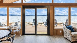 A spacious room with large windows overlooking a body of water, wooden flooring, and a variety of seating arrangements including chairs and a sofa. - Beachfront I Tiki lounge | Pool table | Pinball I Mini Golf (Langley)