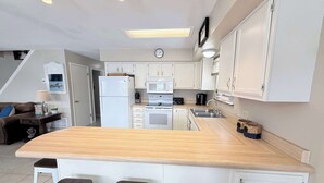 Een moderne keuken met witte kasten, een centraal eiland met krukken, een magnetron, een koelkast en een spoelbak.