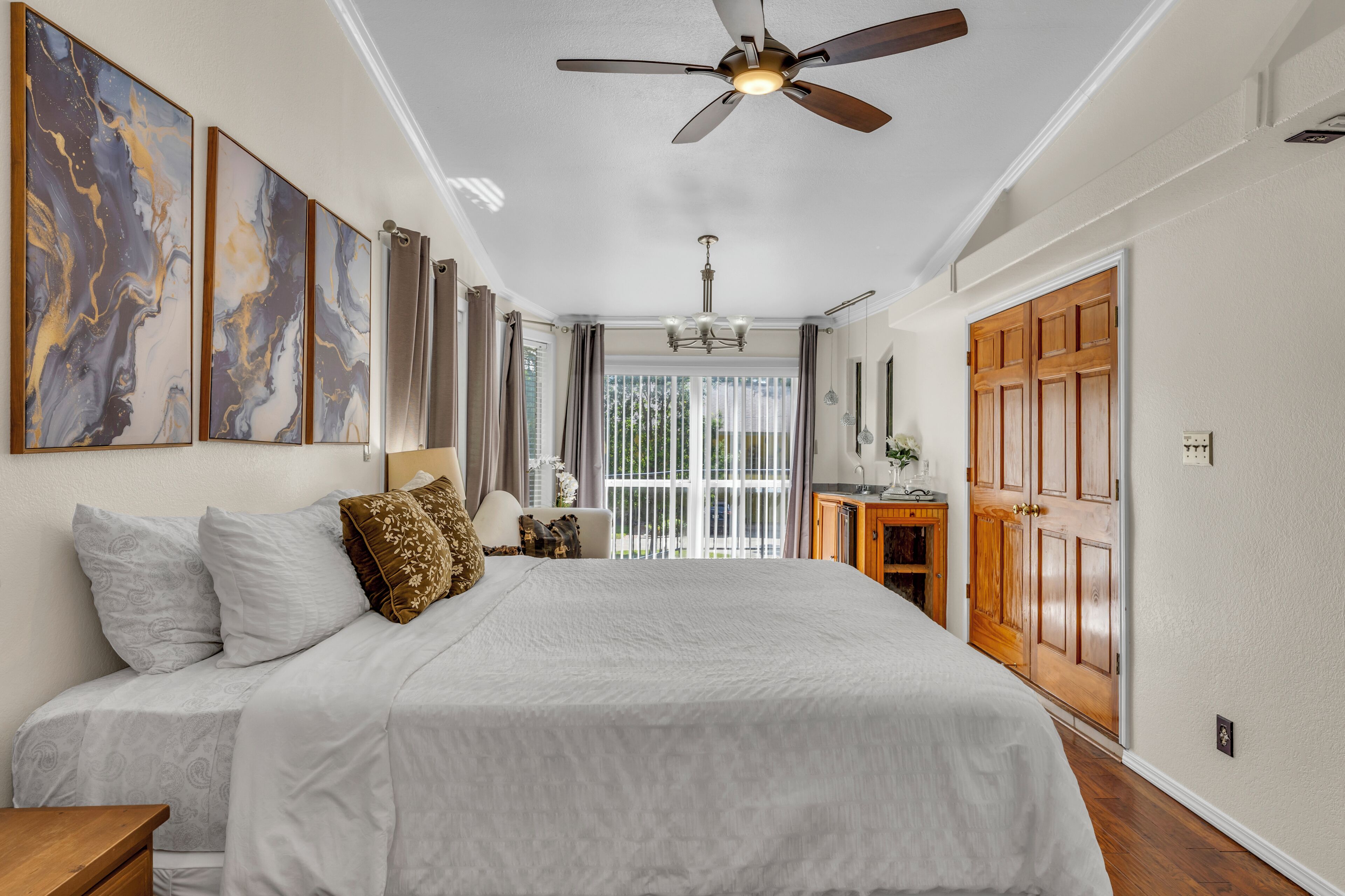 A bedroom with a large bed, a ceiling fan, and a view of the outdoors through a sliding glass door.