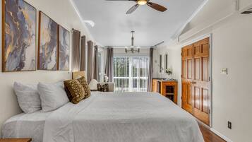 A bedroom with a large bed, a ceiling fan, and a view of the outdoors through a sliding glass door.