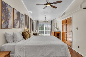 Un dormitorio con una cama grande, un ventilador de techo y vistas al exterior a través de una puerta corrediza de vidrio.