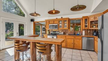A modern kitchen with wooden cabinets, stainless steel appliances, and a large dining table with bar stools.