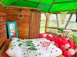 A cozy log cabin room with a bed, a mirror, and a window overlooking greenery.