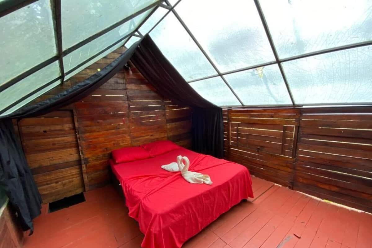 Ein kleiner, gemütlicher Raum mit Holzbalkendecke und einem Bett mit roter Bettdecke.