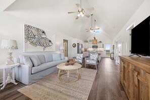 Ein großzügiger Wohnbereich mit einer Couch, einem runden Couchtisch, Deckenventilatoren und einem Fernseher.