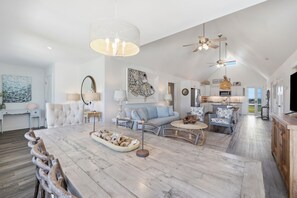Ein großzügiger Wohnbereich mit einem großen Esstisch aus Holz, einer Couch und einer Küche im Hintergrund.