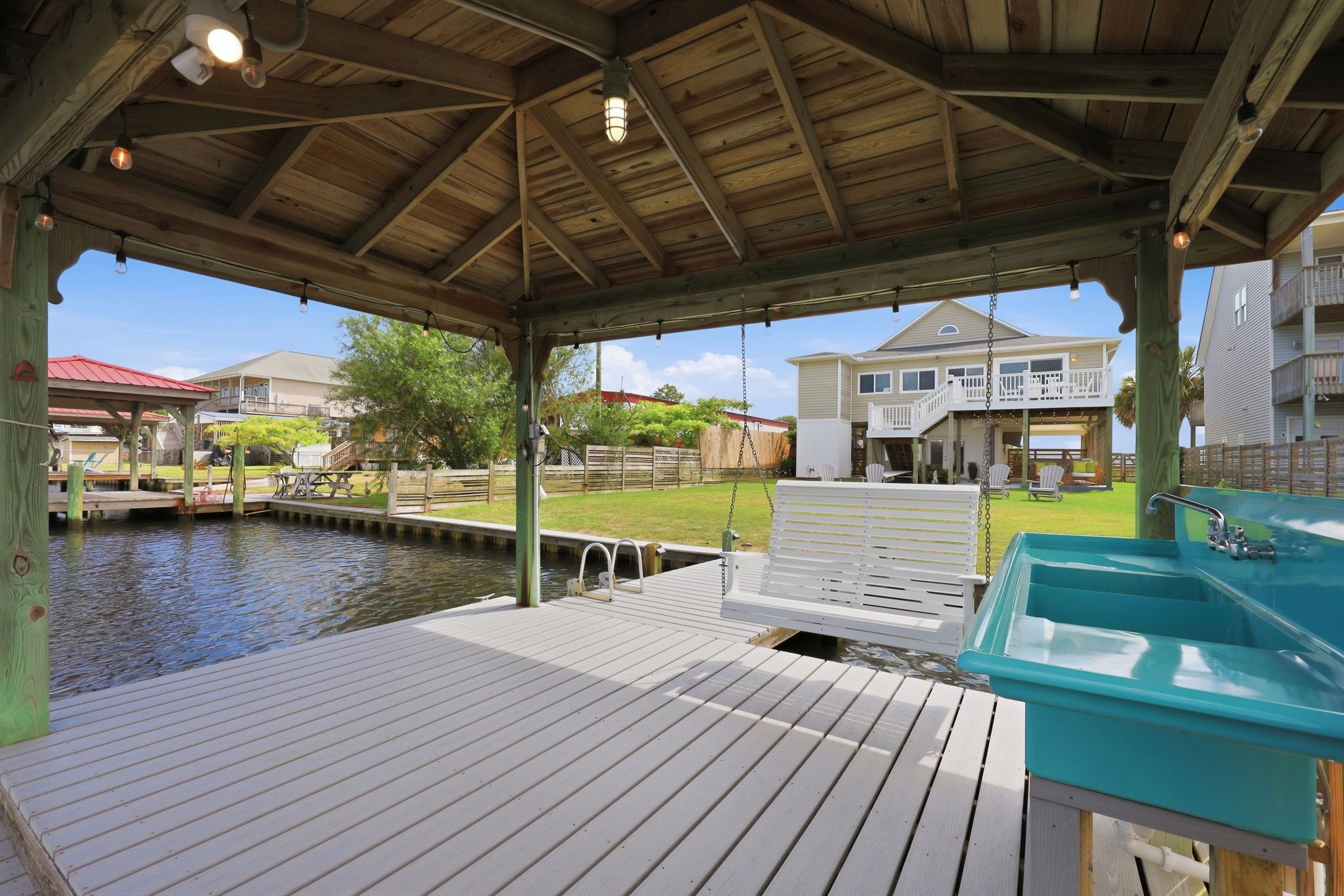 Une terrasse couverte avec une piscine, une chaise longue blanche et un lavabo turquoise.