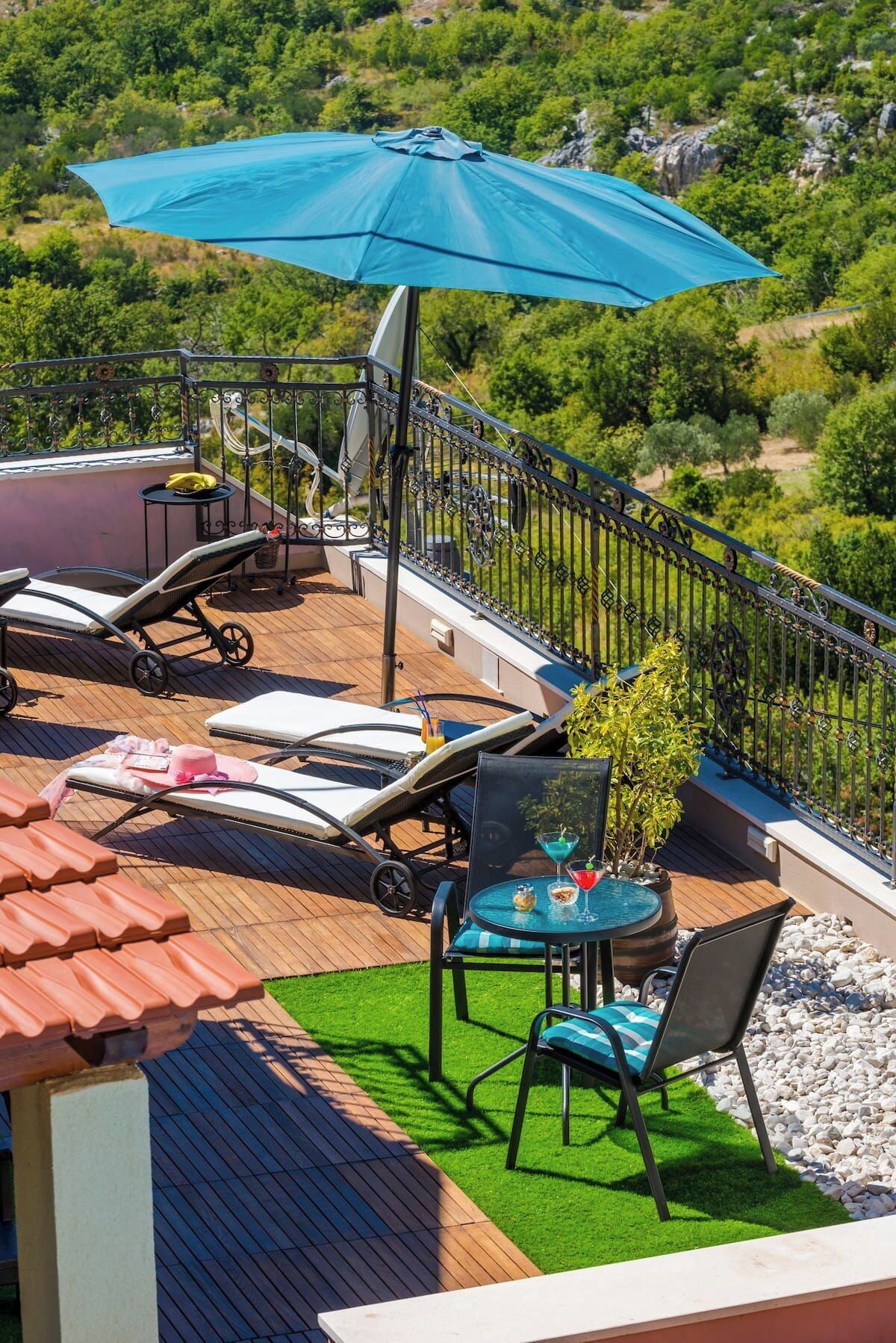 A rooftop terrace with lounge chairs, a table with drinks, and a large umbrella.