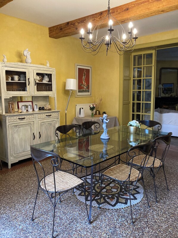 Zona pranzo con tavolo in vetro circondato da sedie in vimini, un lampadario sopra e un mobile con ante in vetro.