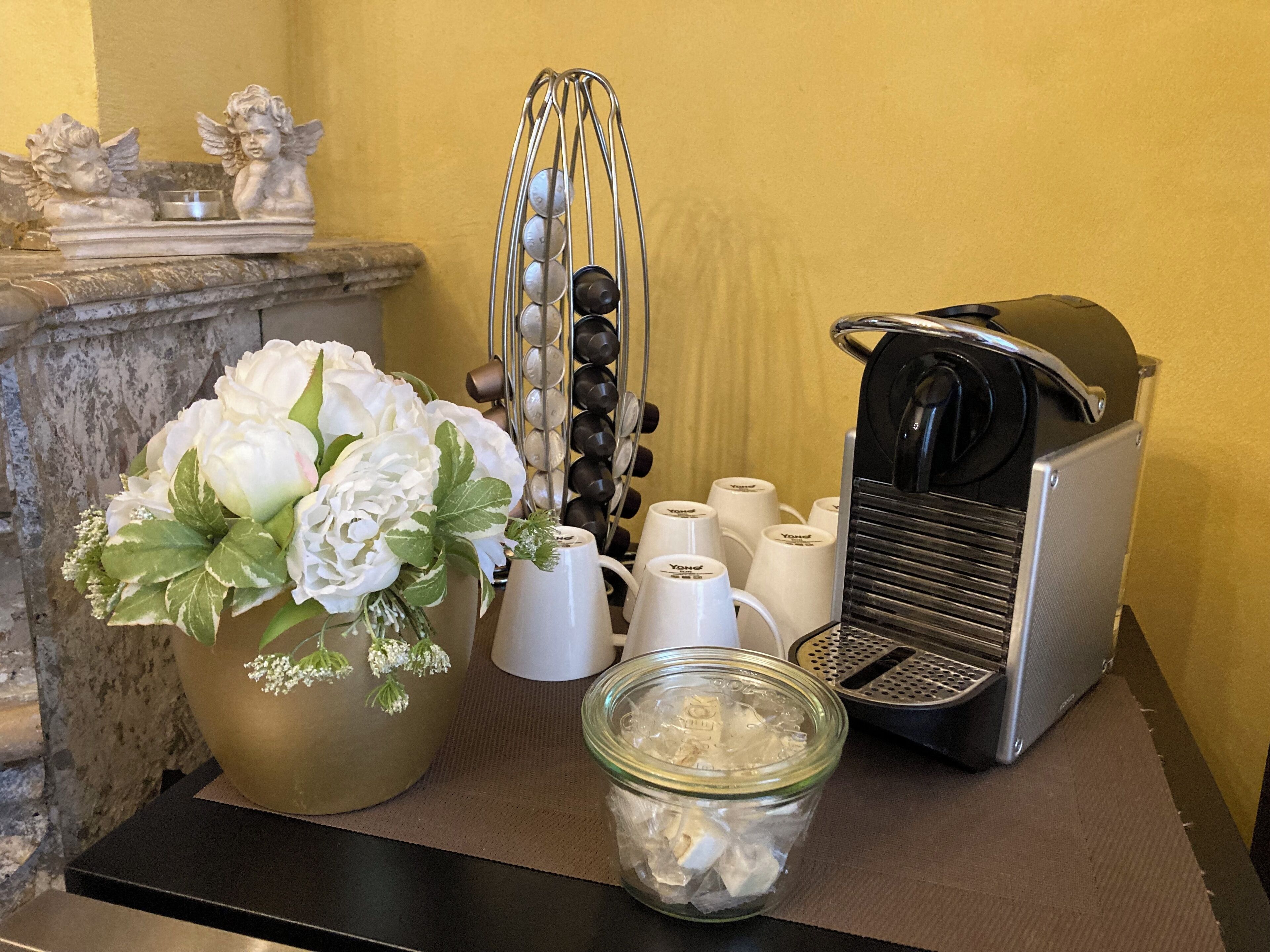 A kitchen counter with a coffee maker, a jar of ice, a flower arrangement, and a metal container with balls.