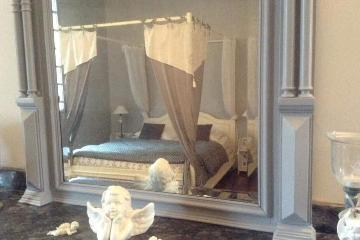 A bedroom with a four-poster bed, a nightstand, and a mirror reflecting the room.