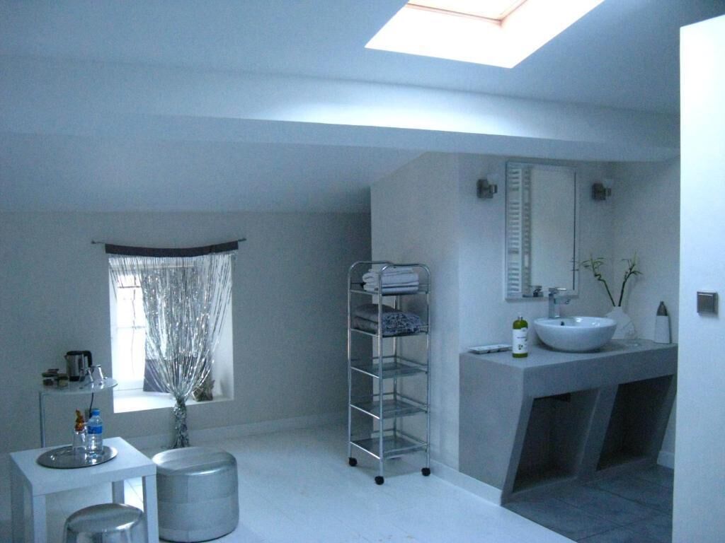 Une salle de bain moderne avec un puits de lumière, un grand miroir, un lavabo blanc et une étagère en métal où sont posées des serviettes.