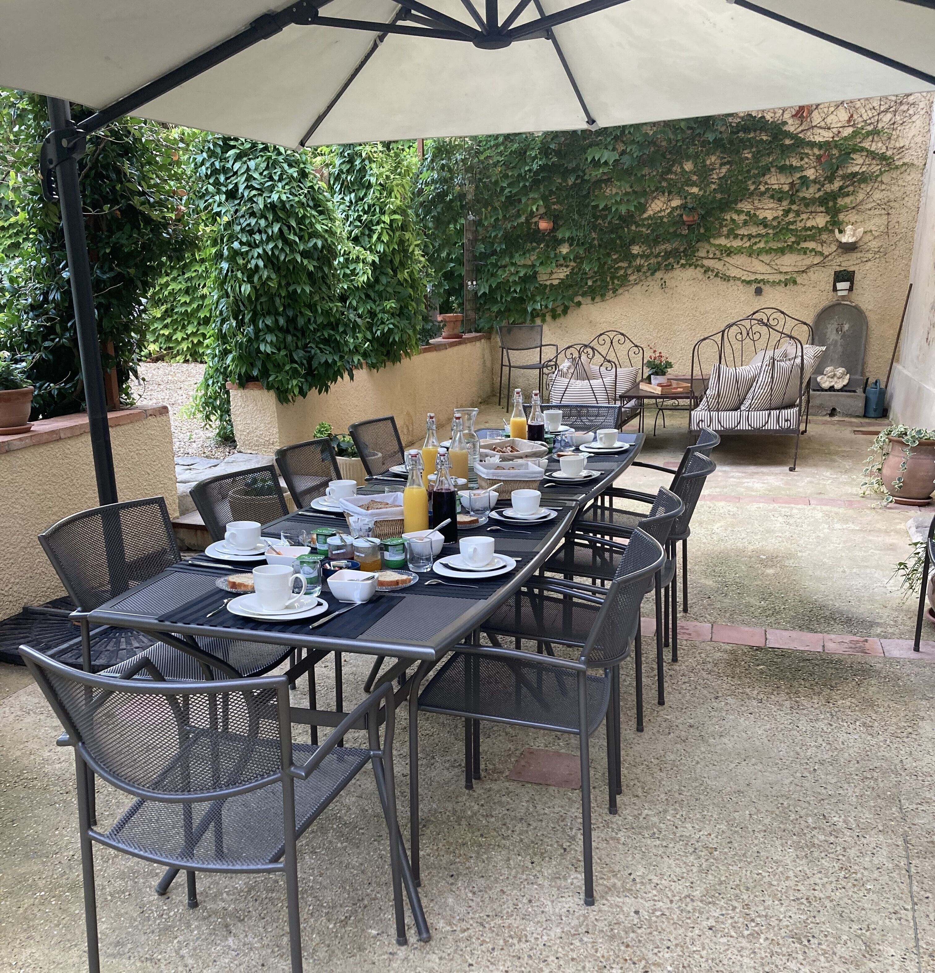 Un espacio exterior para comer bien organizado, con una mesa larga dispuesta para el desayuno, rodeada de sillas y una sombrilla.