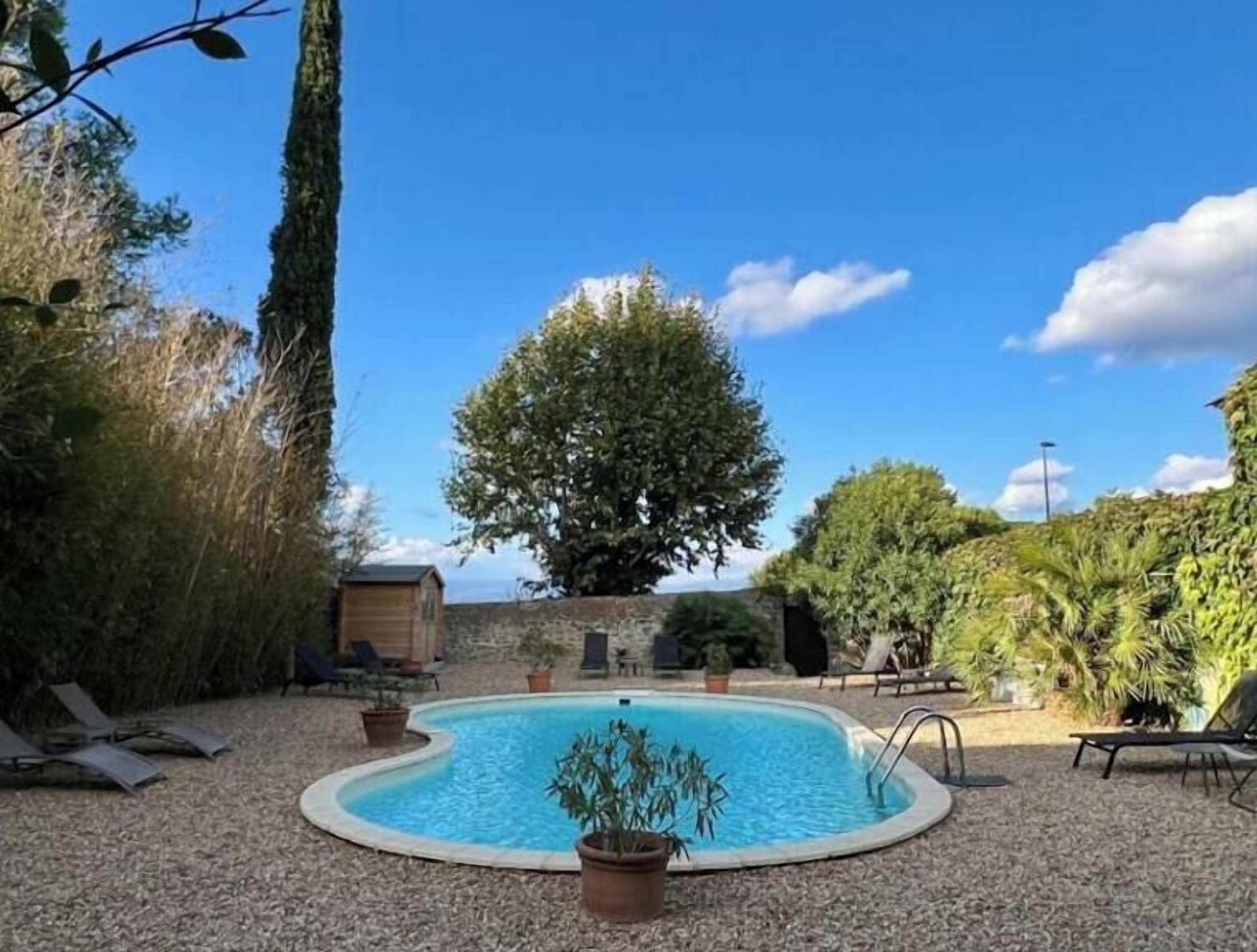 Ein Schwimmbecken, umgeben von Kies, mit einer Holzterrasse und Liegestühlen.