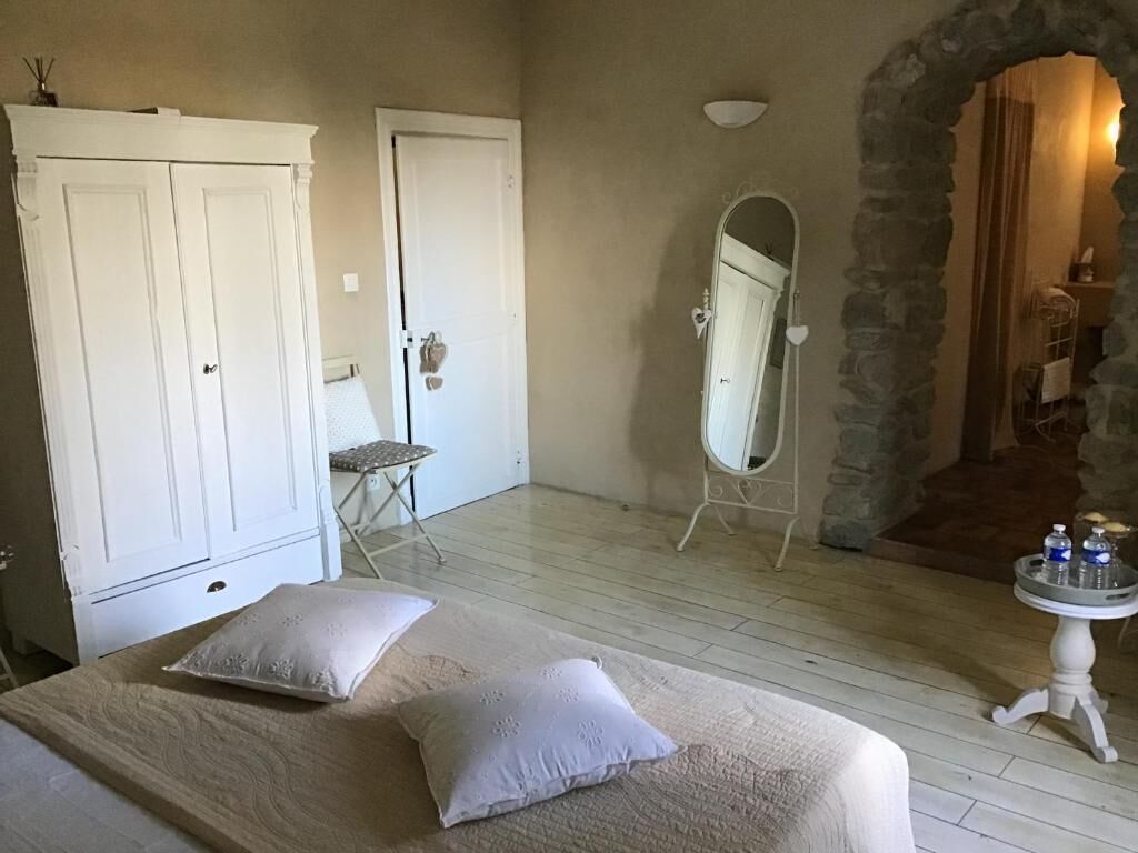 Ein Schlafzimmer mit einem Bett, zwei Kissen, einem Kleiderschrank, einem Spiegel und einem kleinen Tisch mit Gegenständen darauf.