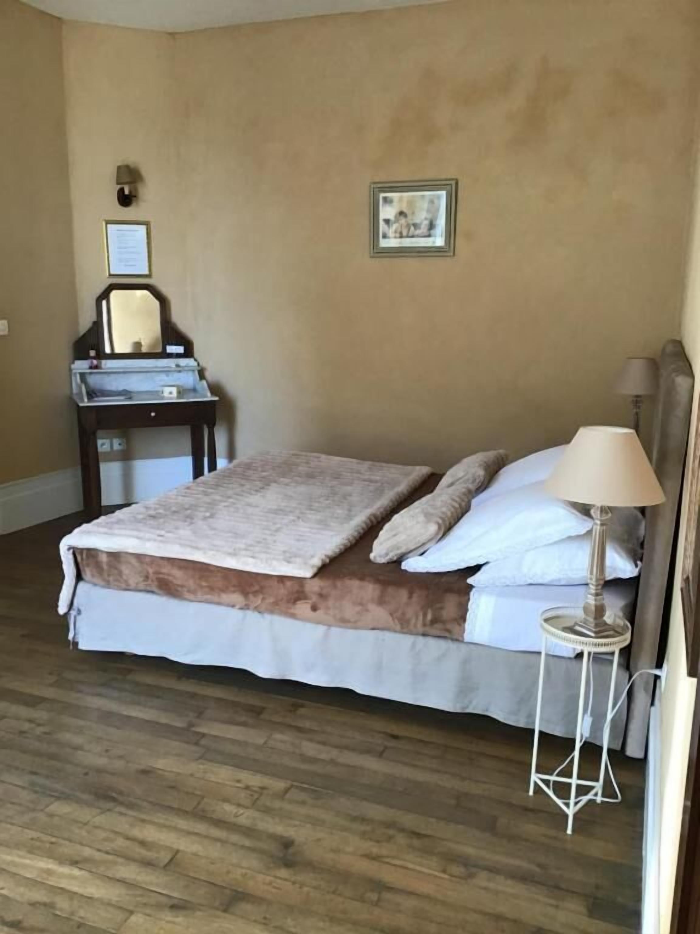 Quarto com cama, mesa de cabeceira, luminária e pequena escrivaninha com espelho.