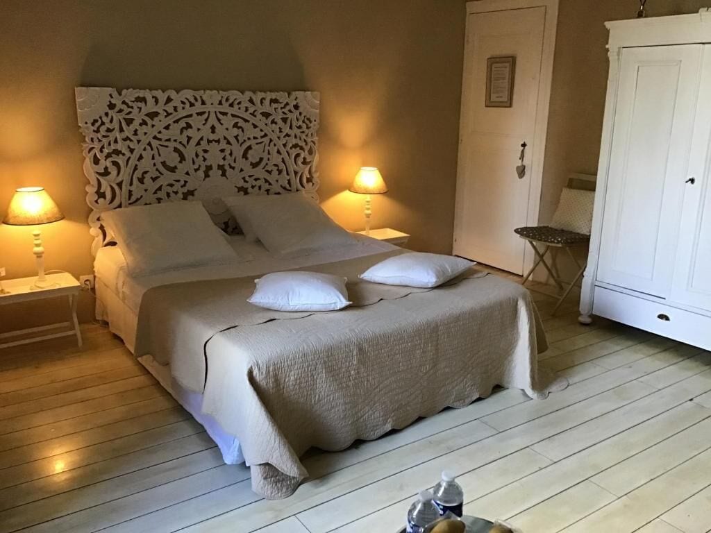 Un lit bien fait, agrémenté d’une tête de lit décorative, de deux lampes de chevet et d’une armoire blanche.