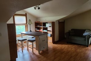 Una habitación acogedora con un escritorio, dos sillas, una estantería y un sofá verde.
