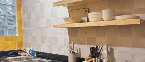 A kitchen with a granite countertop, wooden cabinets, and a window with blinds.