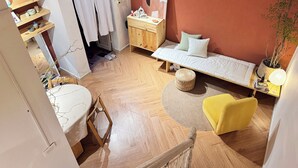 Une petite chambre à coucher accueillante, avec un plancher en bois, un lit avec des oreillers, une table de chevet, une chaise et une plante en pot.