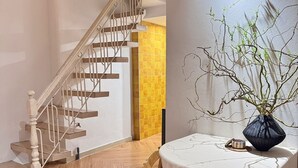 Un escalier avec des marches en bois et des rampes en métal, une table ronde recouverte d’une nappe blanche et un vase orné de branches.