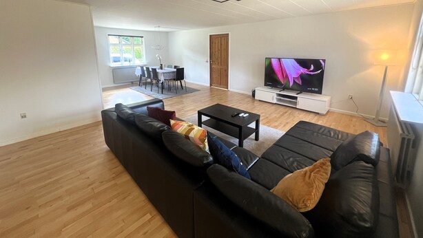 Una sala de estar moderna con un sofá de cuero negro, un televisor de pantalla plana y una zona de comedor con una mesa y sillas.