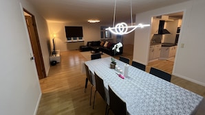 Una cocina moderna con horno integrado, un comedor con una mesa dispuesta para dos personas y una sala de estar con sofá y televisor.