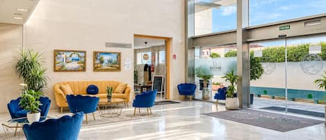 Um hall moderno com um sofá amarelo, poltronas azuis e uma porta de vidro que dá para o exterior.