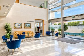 A modern lobby with a yellow sofa, blue armchairs, and a glass door leading outside. - GuestReady - Domocenter studio with garage (Bormujos)