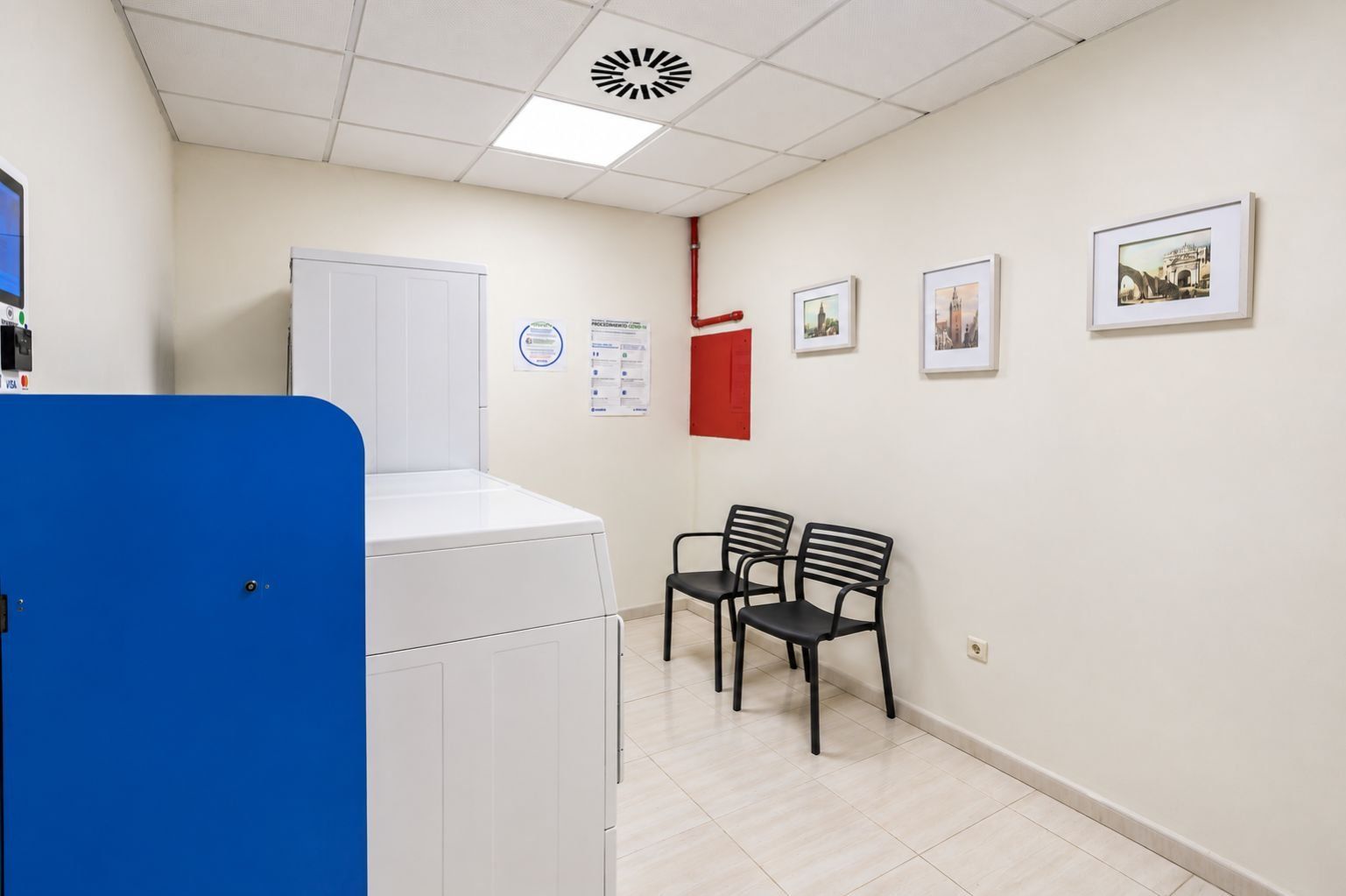 A room with a washing machine, two chairs, a red cabinet, and framed pictures on the wall.