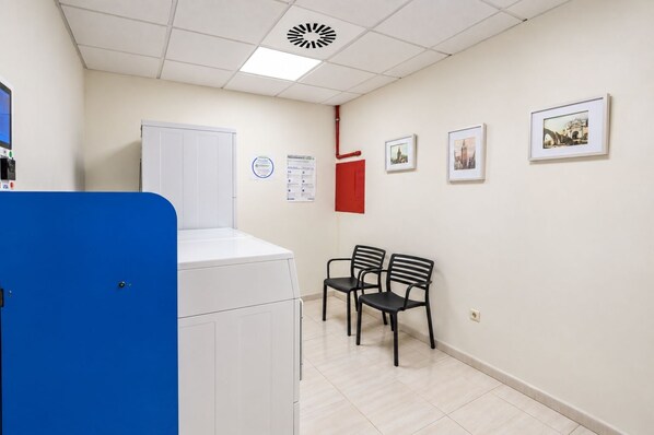 A room with a washing machine, two chairs, a red cabinet, and framed pictures on the wall. - GuestReady - Domocenter studio with garage (Bormujos)