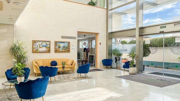 A modern lobby with a yellow sofa, blue chairs, and a glass entrance. - GuestReady - Domocenter studio with garage (Bormujos)