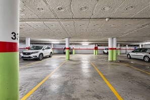 A multi-level parking garage with cars parked in designated spaces, concrete pillars with numbers, and a textured ceiling. - GuestReady - Domocenter studio with garage (Bormujos)