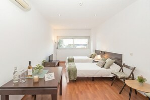 Une chambre d’hôtel moderne avec un grand lit, une petite table avec des verres et des bouteilles de vin, une chaise et une fenêtre donnant sur un beau paysage.