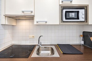 A modern kitchen with a built-in microwave, a stainless steel sink, and a black induction cooktop. - GuestReady - Domocenter studio with garage (Bormujos)