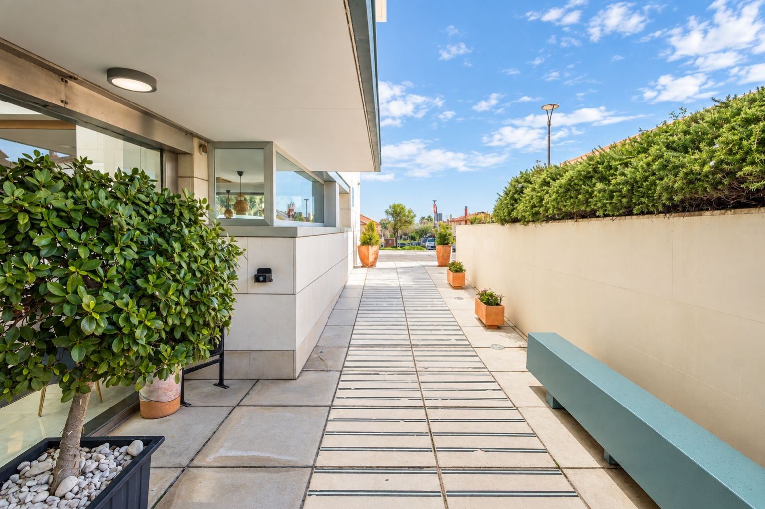 Un bâtiment moderne doté d’une passerelle couverte, de plantes en pot et surplombant un ciel dégagé.