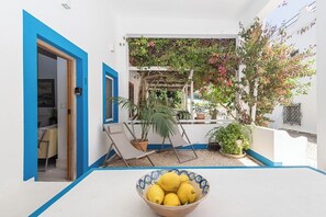 Een wit gebouw met blauwe accenten, een overdekt terras met een tafel en stoelen, en een schaal met citroenen.