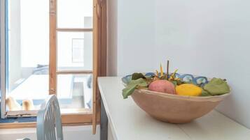 Een kamer met een raam met houten kozijn, een witte tafel en een schaal met fruit.
