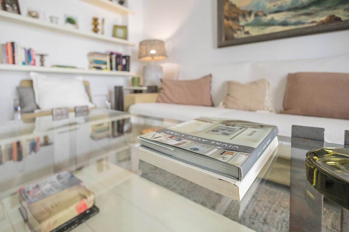 Een moderne woonkamer met een glazen salontafel, een witte bank en een boekenkast.