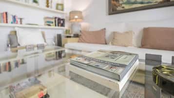 Een moderne woonkamer met een glazen salontafel, een witte bank en een boekenkast.