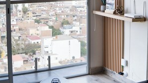 Ein modernes Zimmer mit großem Fenster, einer Wand aus Holzleisten, einem runden Spiegel und einer schlichten Leuchte.
