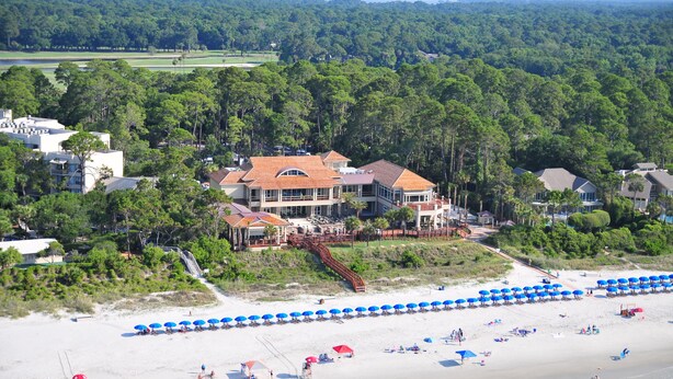 Une propriété située sur la côte, avec une grande maison, des parasols de plage et un accès à la plage.