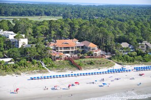 Ein Küstenanwesen mit einem großen Haus, Strandstühlen und einem Strand.
