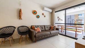 A modern living room with a brown leather sofa, two black mesh chairs, and decorative wall art. - APTO Próximo à Praia | Barra de São Miguel | San Martin | Destino BSM 106A (Barra de São Miguel)